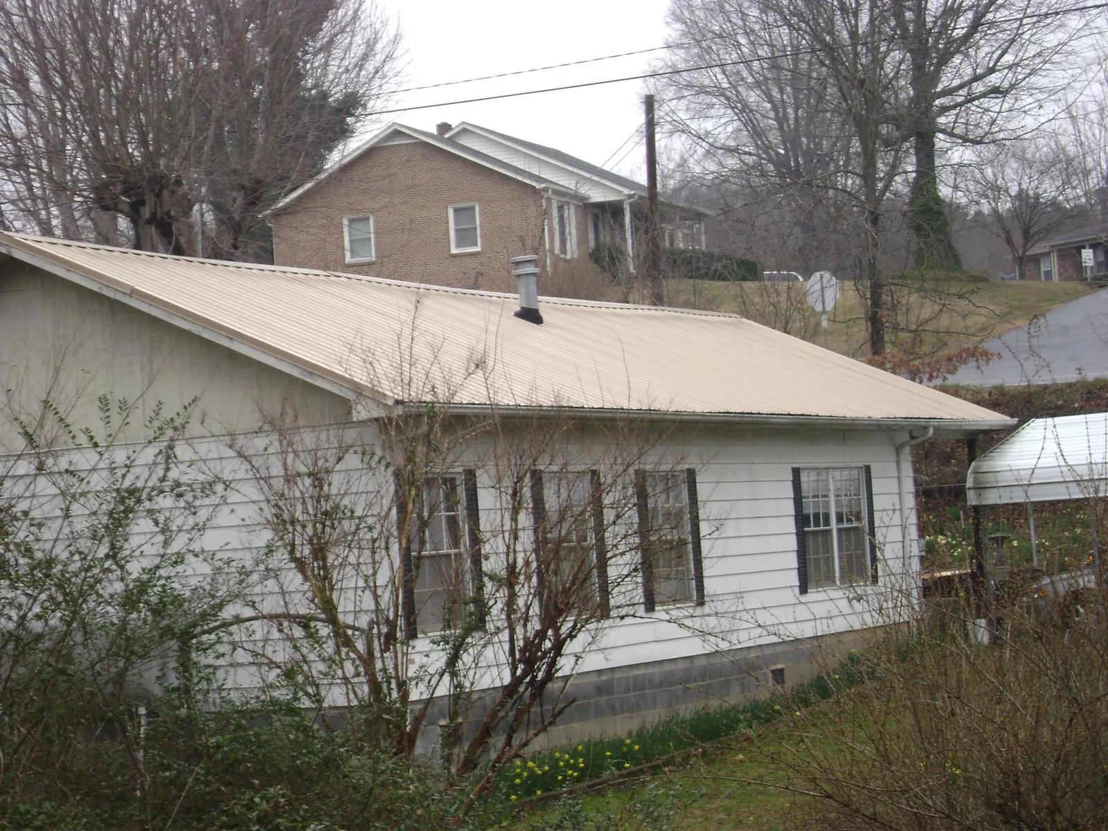 Tan metal roof on a white sided house set into a hillside — Commercial Roofing by Roofing Brothers in Blackwood